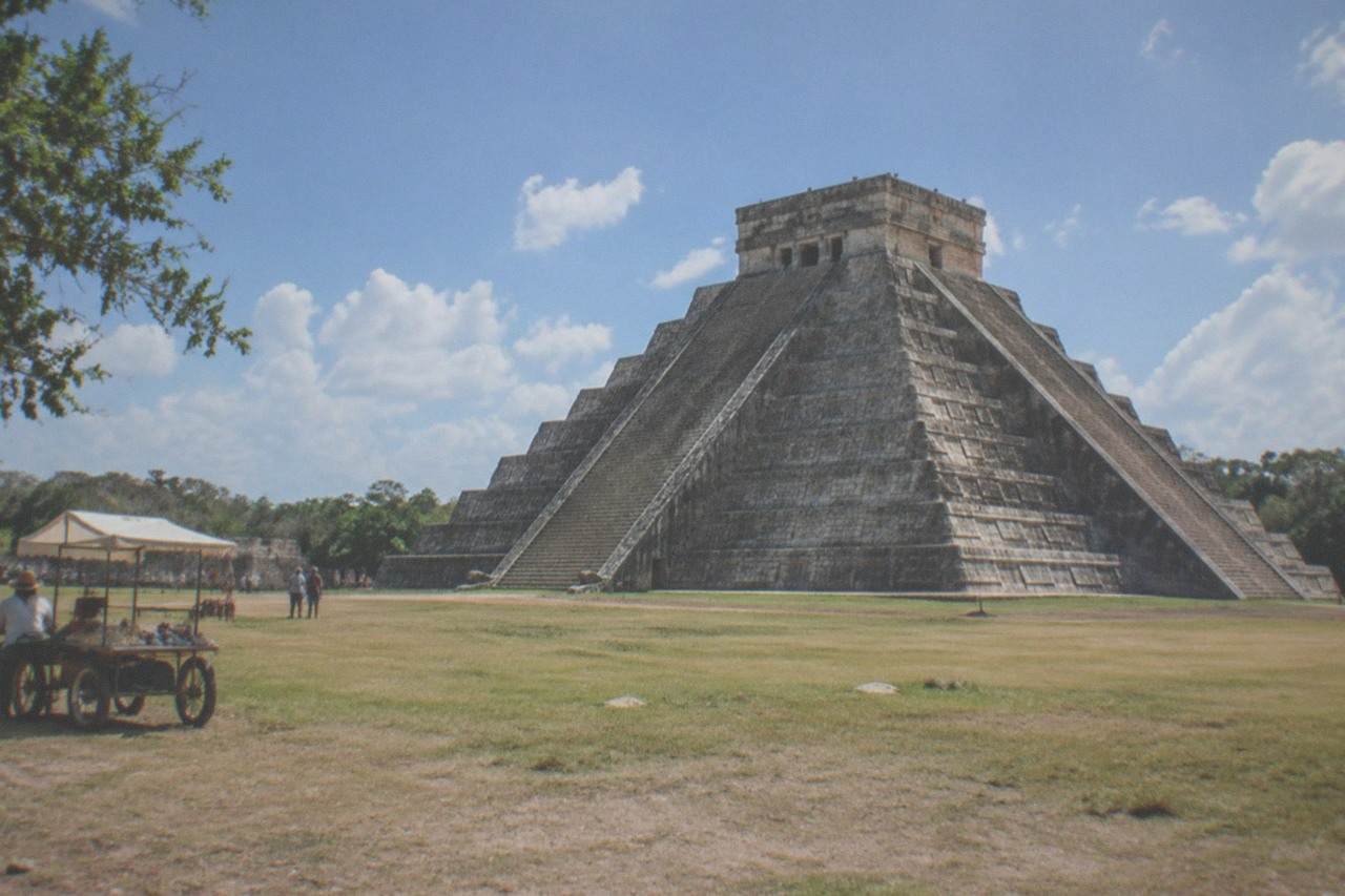 El Castillo pyramid at Chichen Itza rising above a wide grassy plaza under a bright sky