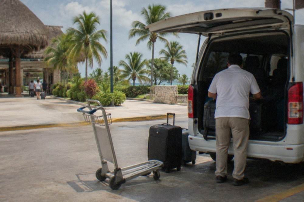Private transfer van parked at a tropical airport curb with luggage being loaded