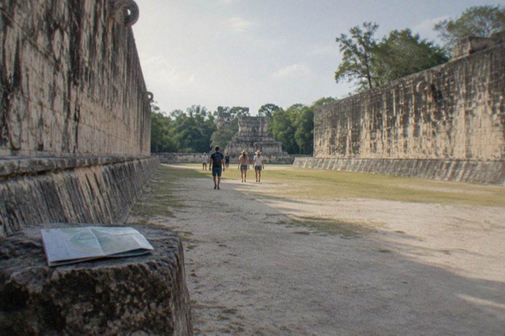 A wide stone ball court corridor bordered by carved walls and low jungle canopy