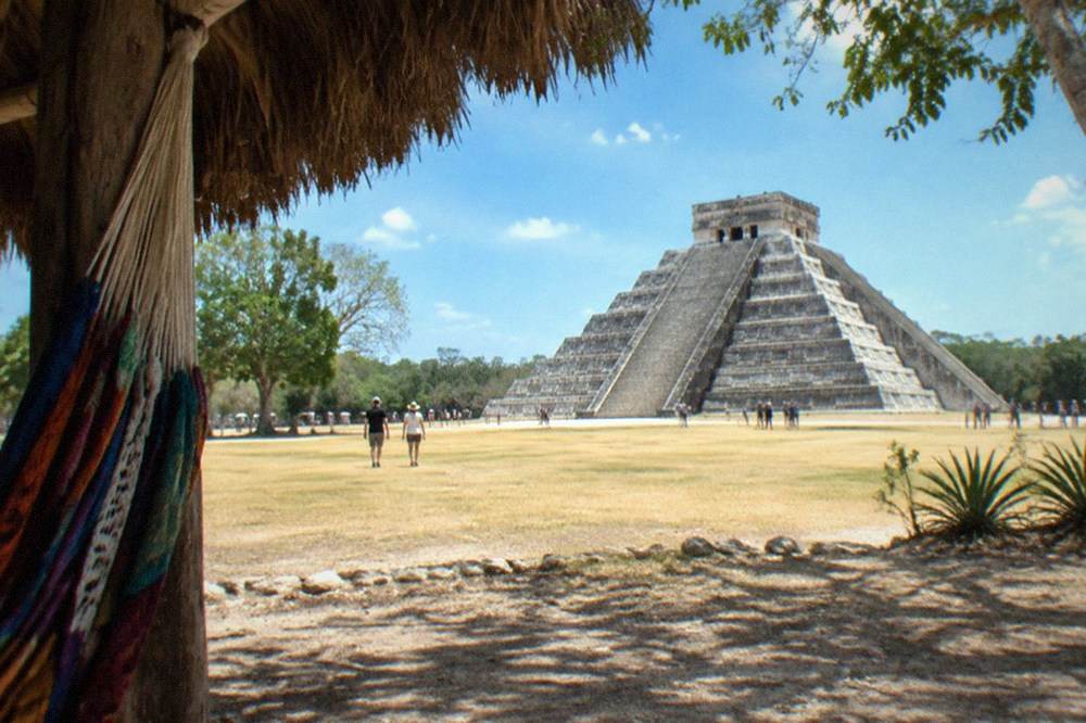 The step pyramid of Chichen Itza under a wide blue sky with dry grass in the foreground