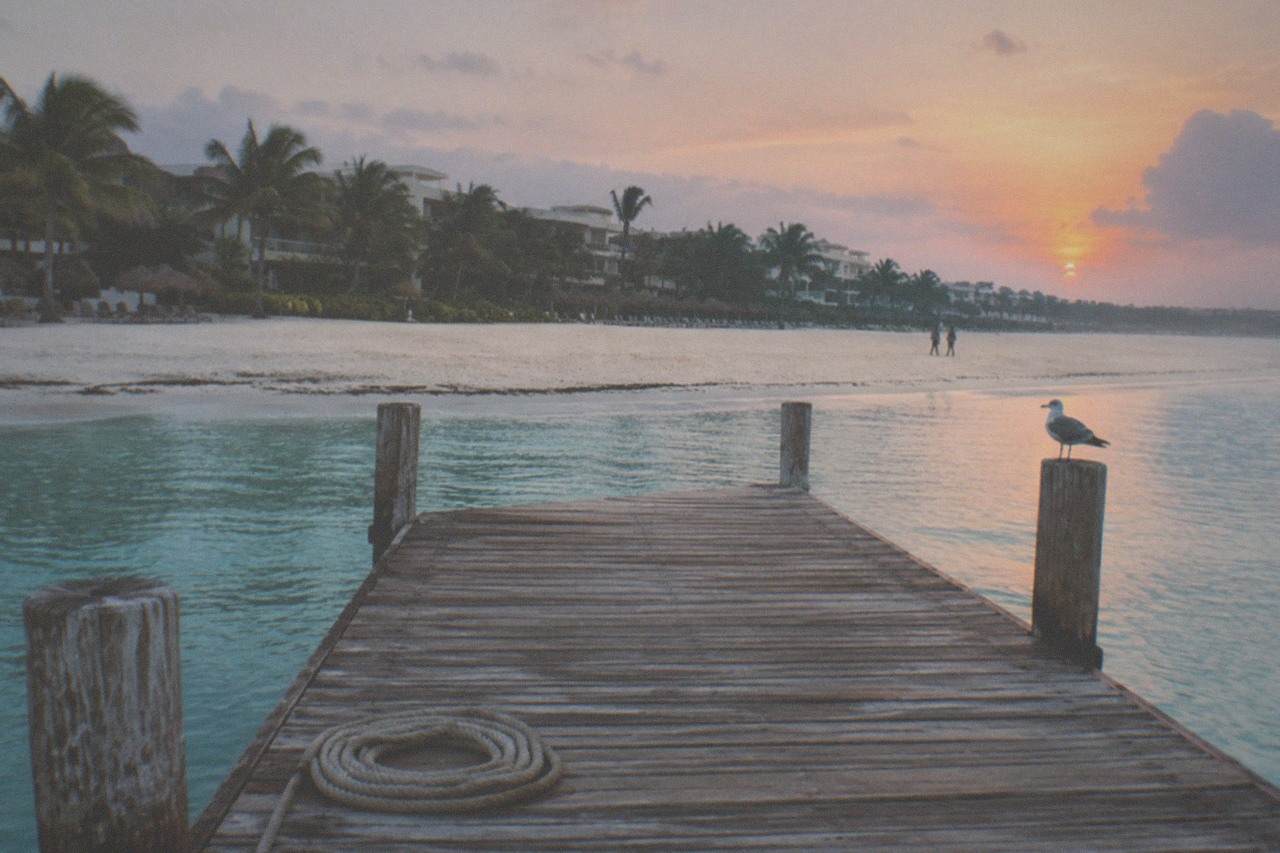 Empty beach with turquoise water and a wooden dock at sunrise
