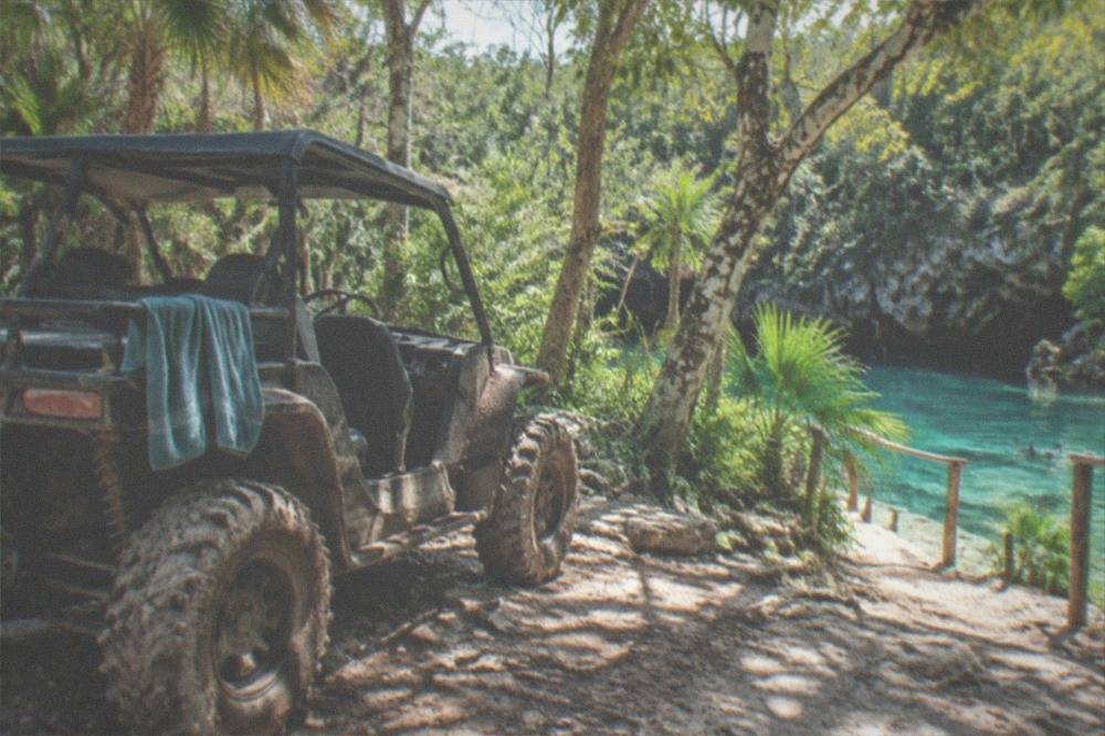 Open-air buggy parked on a jungle trail beside a turquoise cenote