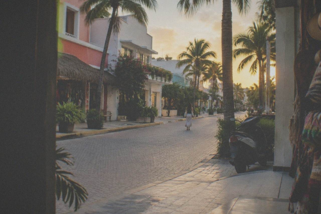 Fifth Avenue pedestrian street in Playa del Carmen at golden hour with shopfronts and palm trees