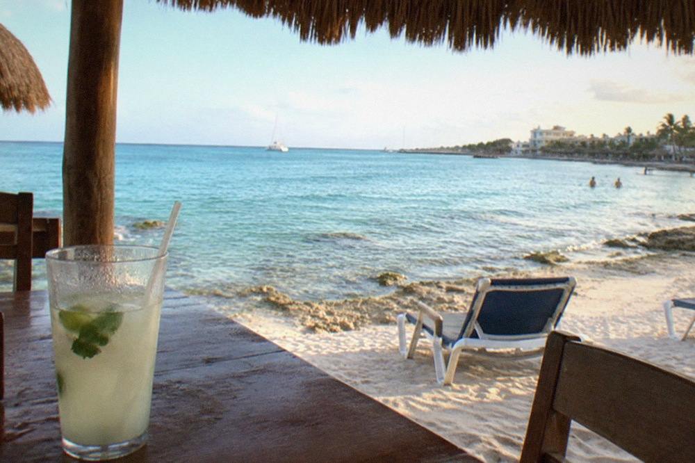 Quiet beach club shoreline near downtown Cozumel with calm turquoise water and thatched shade structures
