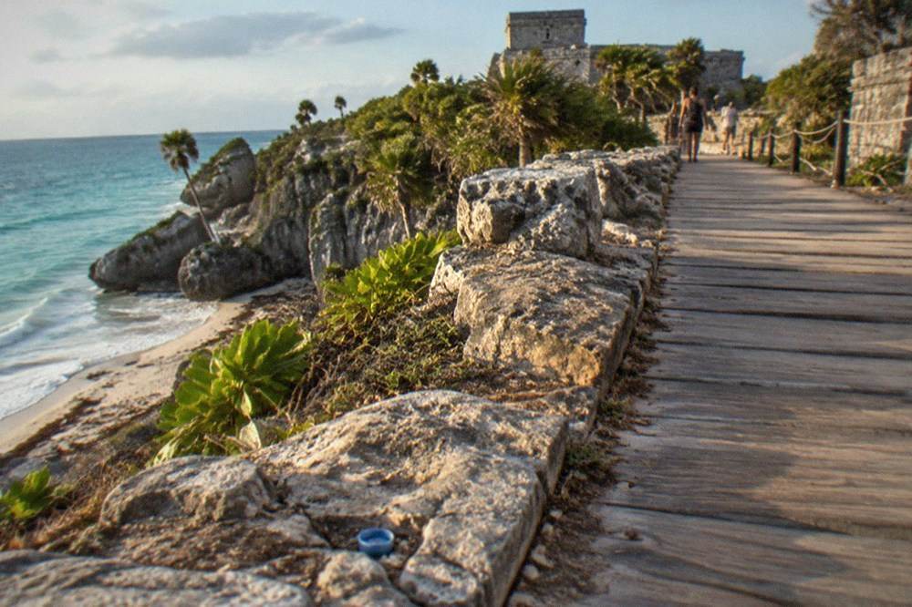 Stone Maya temple walls and wooden barrier walkways along the clifftop path at the Tulum archaeological zone