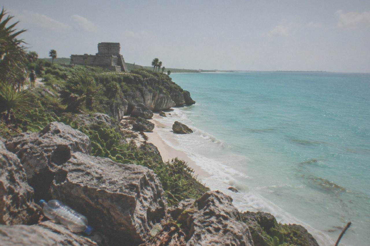Tulum cliffside ruins overlooking a calm turquoise Caribbean bay at midday