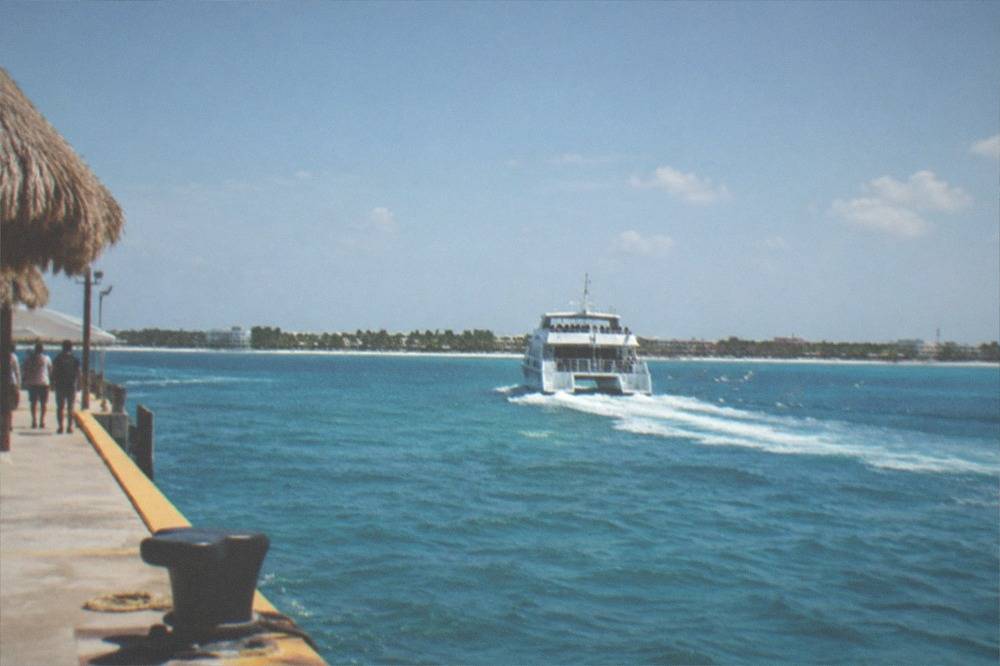 A passenger ferry cruising across open water toward an island coastline in bright daylight
