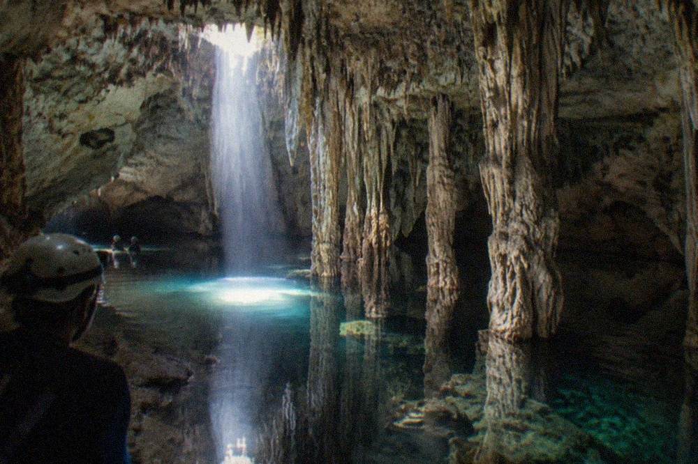 Underground cave cenote with still clear water and rock formations lit by a shaft of daylight