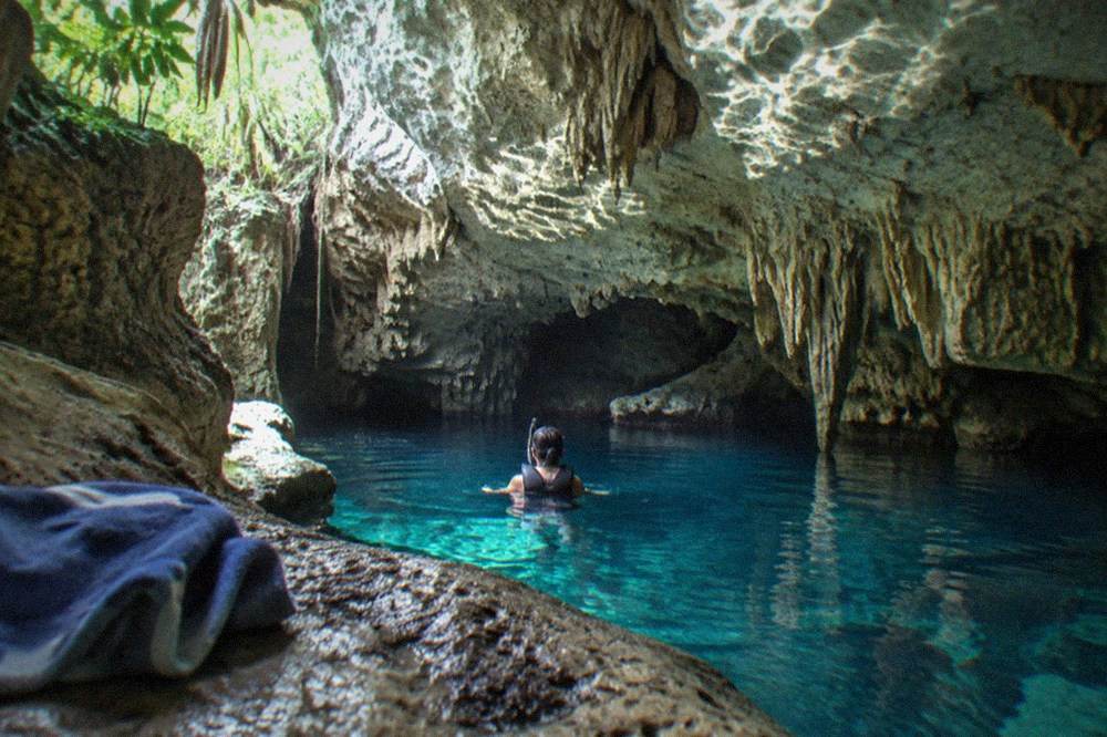 Swimmer with mask and life vest floating in clear cenote water between rock walls