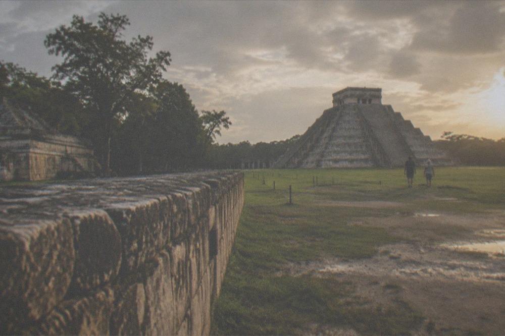 Low stone ruins of Chichen Itza in golden late afternoon light with few visitors on the paths
