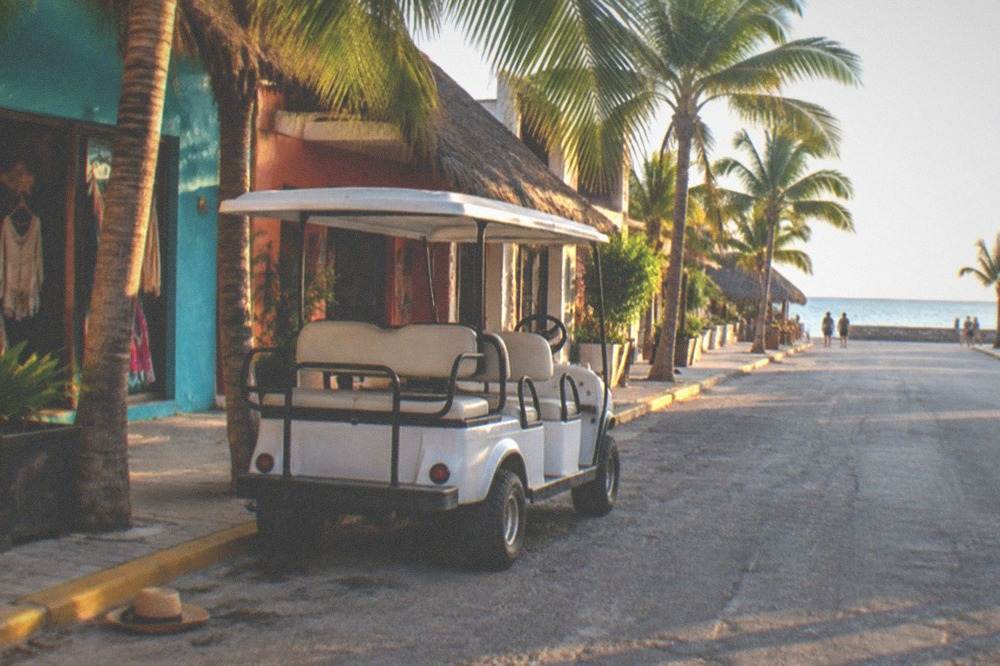 Open-air taxi and colorful storefront on a sunny island street near the waterfront