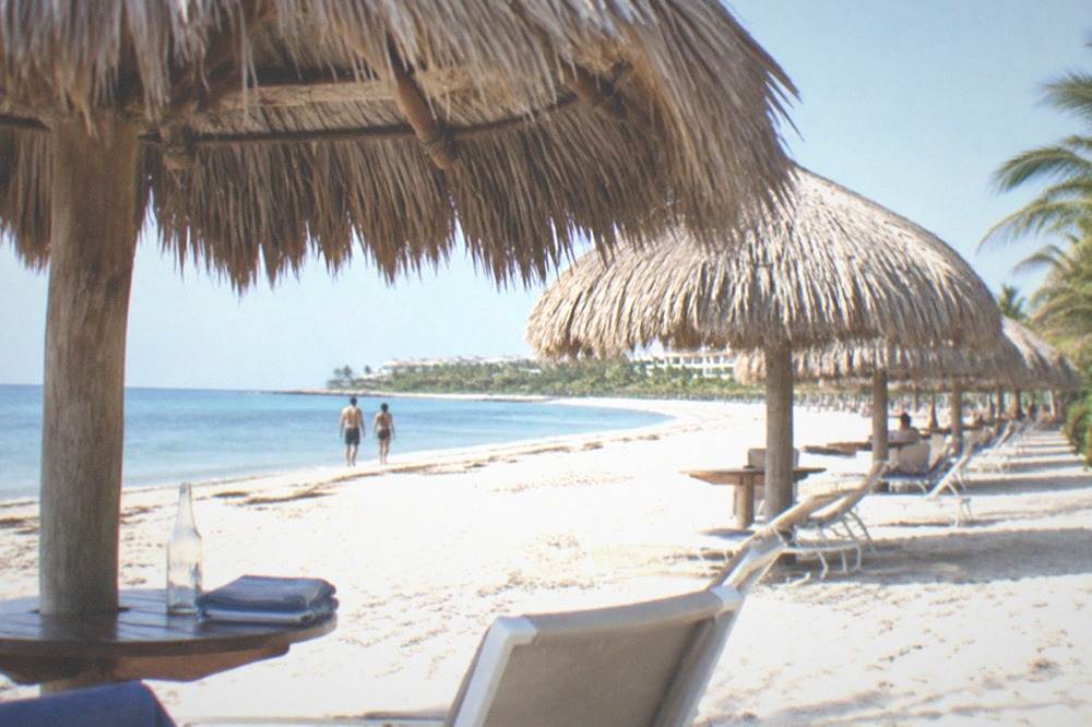 Thatched-roof beach palapas on a wide sandy shore under a clear sky