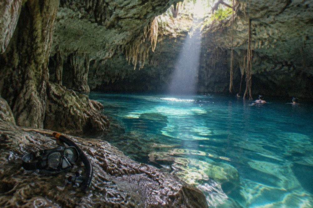 A cavern freshwater pool lit by a shaft of daylight through an opening in the rock ceiling