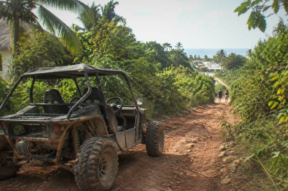 A jungle buggy parked on a dirt track beside dense green vegetation near Playa del Carmen